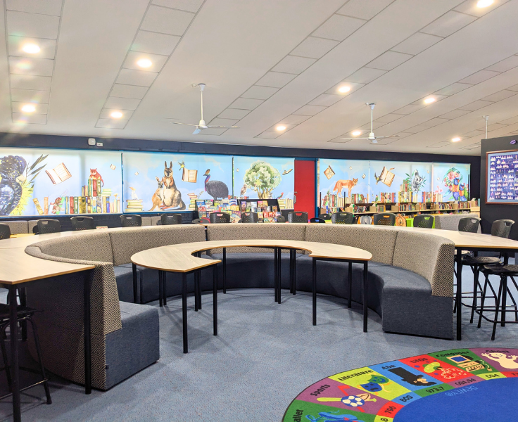 A half circle desk with bench seat in the library with a colourful background.