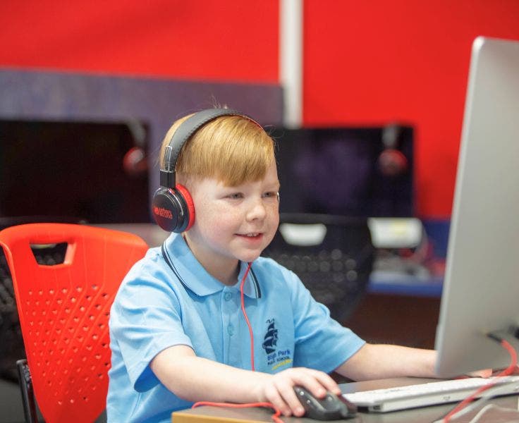 A student with headphones on, looking at a computer screen and doing work.