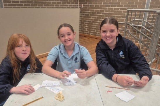3 students sitting at a desk writing notes, preparing for their debating challenge