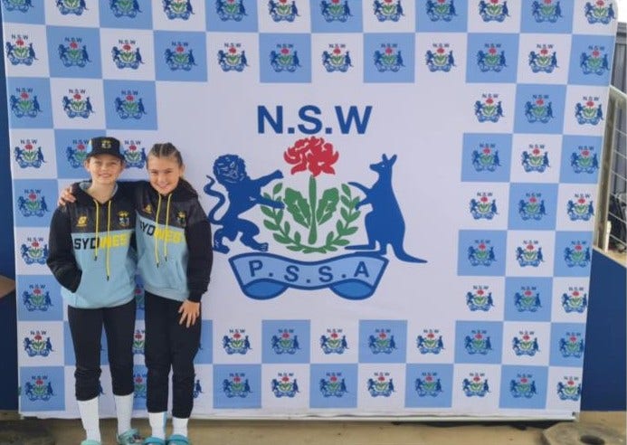 2 students standing in front of a NSW PSSA sign at an athletic event