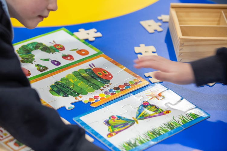 A student partially visible in the photo looking at puzzles on a table.