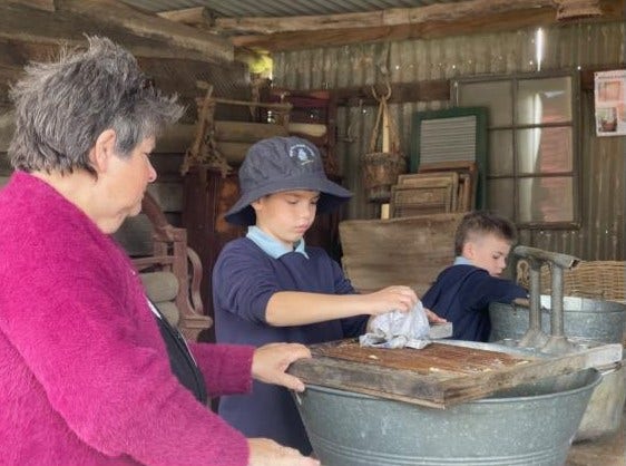 A student cleaning an antique item, whilst a lady watches, at the Australian Pioneer Village when they went on an excursion